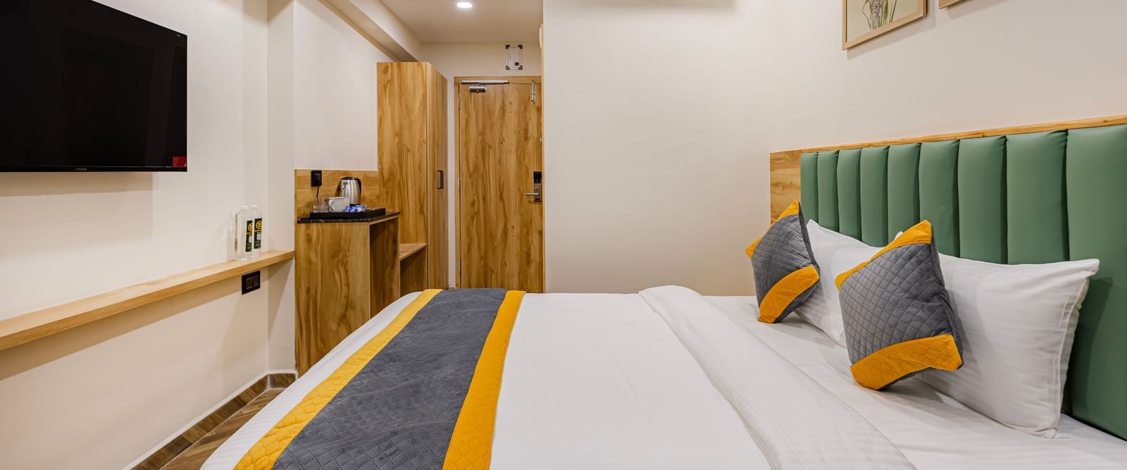 A room at Lemonridge Hotels, KPHB featuring a plush bed with framed wall hangings over it facing the TV mounted on the wall and an air-conditioner mounted on the wall next to it 